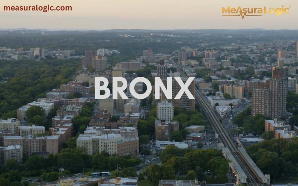 Wide aerial shot of a dense residential New York, Bronx, neighborhood with green trees and an elevated train track.