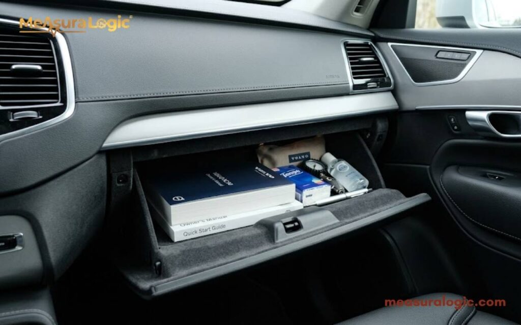 A 12 inches open car glove compartment containing an owner's manual, tissues, and a small pouch.