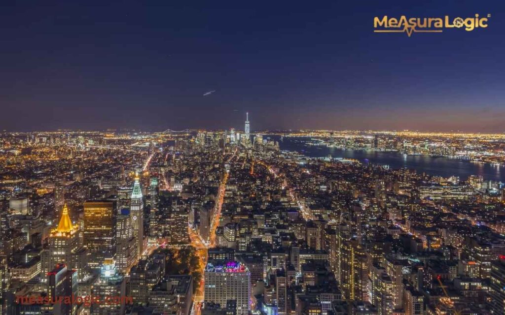 High-angle night view of a glowing New York with the One World Trade Center in the distance.