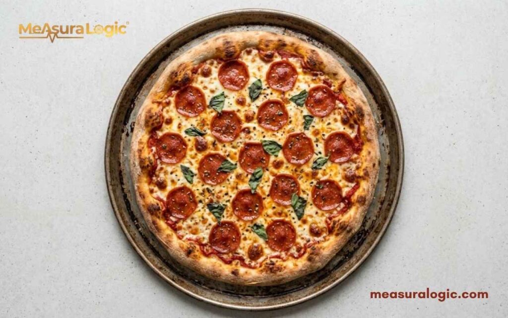 A whole pepperoni pizza with melted cheese and fresh basil leaves on a round baking tray.