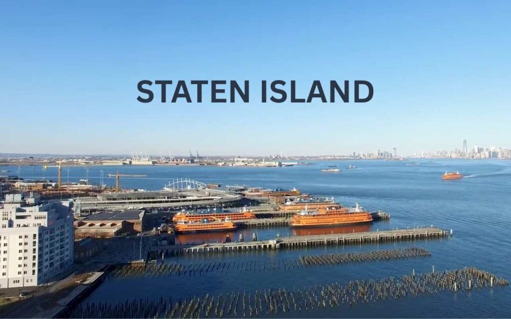 Daytime aerial view of the Staten Island Ferry terminal with orange ferries docked in the blue harbor.