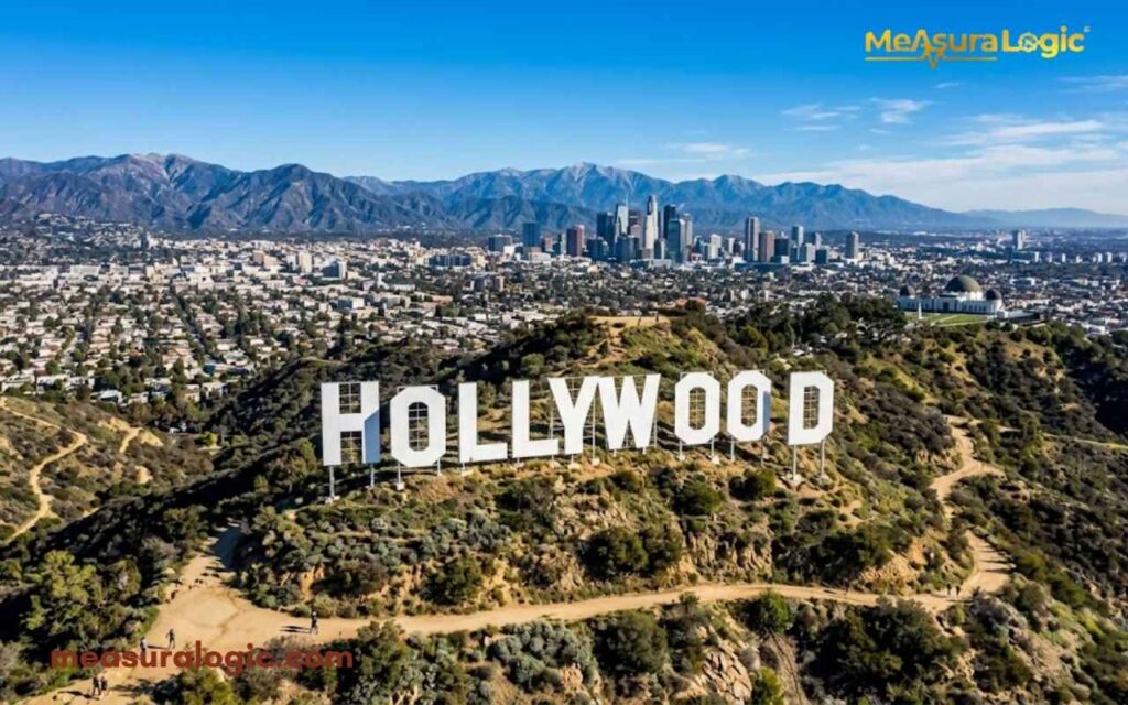The famous Hollywood sign rests firmly on a sunny, rugged hill. You'll spot the vast Los Angeles skyline right behind it.