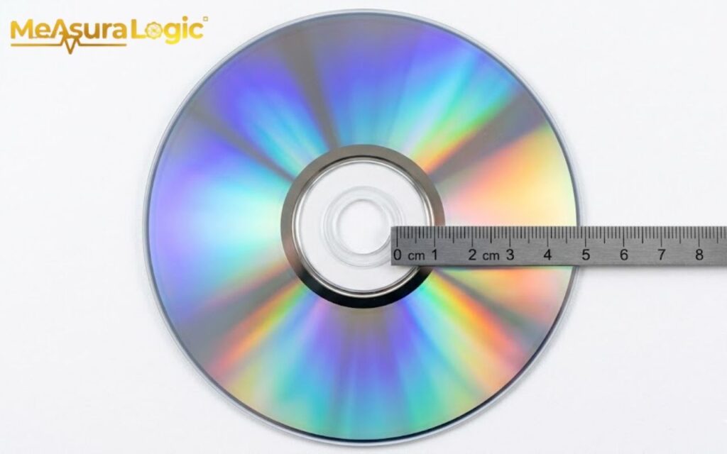 Overhead view of an iridescent CD. A metal ruler lies across the disc's surface, measuring in centimetres.