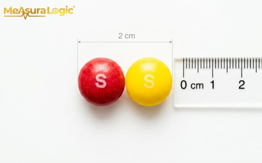 A red Skittle and a yellow Skittle are measured by a ruler. The candies are 2 cm wide.