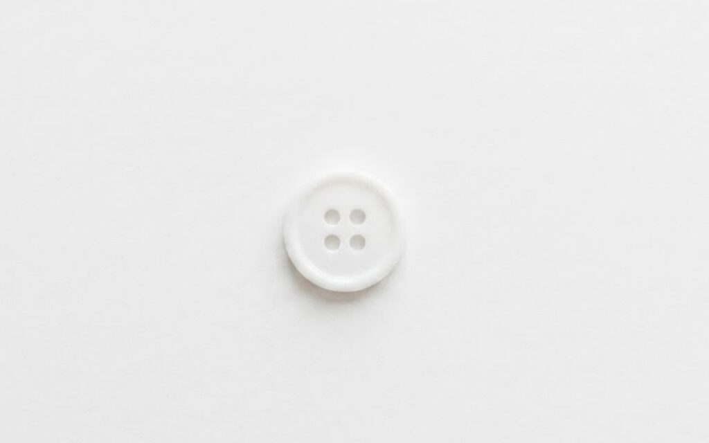 A single white, four-hole shirt button.
Centered against a plain white background.
