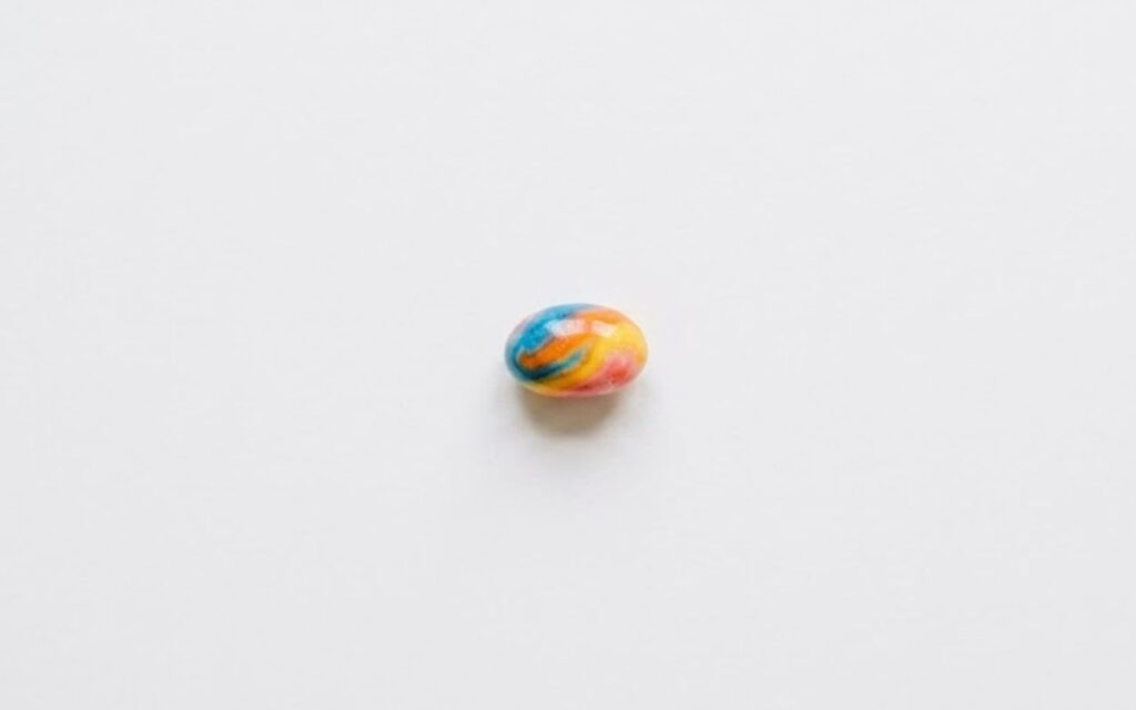 A single multi colored 1 gram swirling candy, centered on a plain white background.