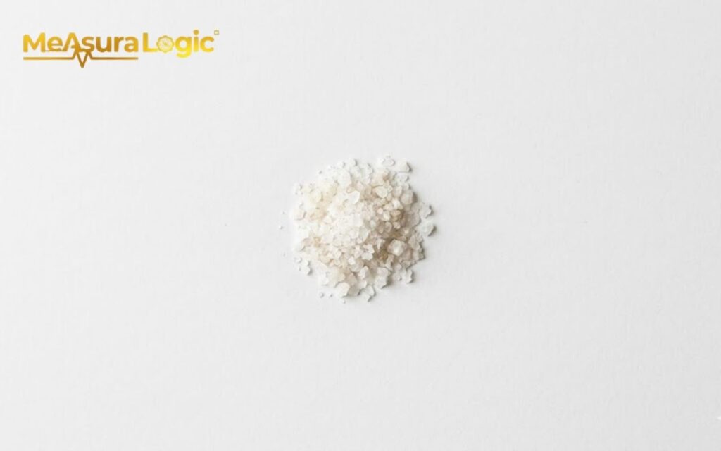 A centered pile of coarse, off-white sea salt crystals on a white background.
