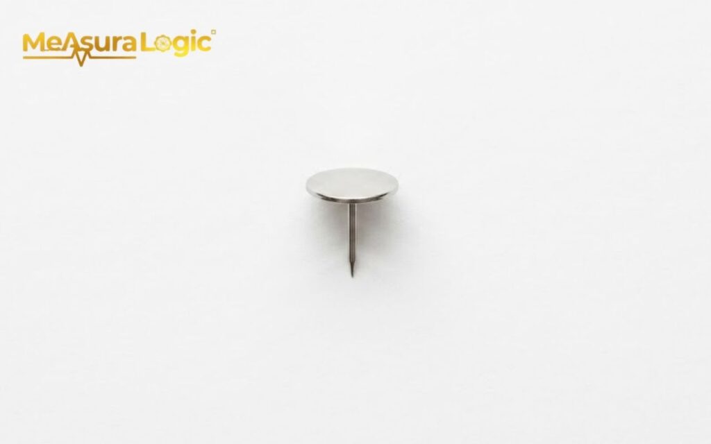A single silver thumbtack standing upright on its sharp point.